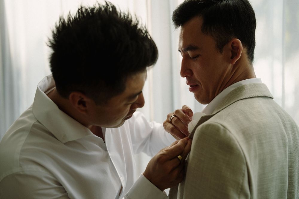 Groomsmen in white shirts and light suits getting ready together in a bright room.