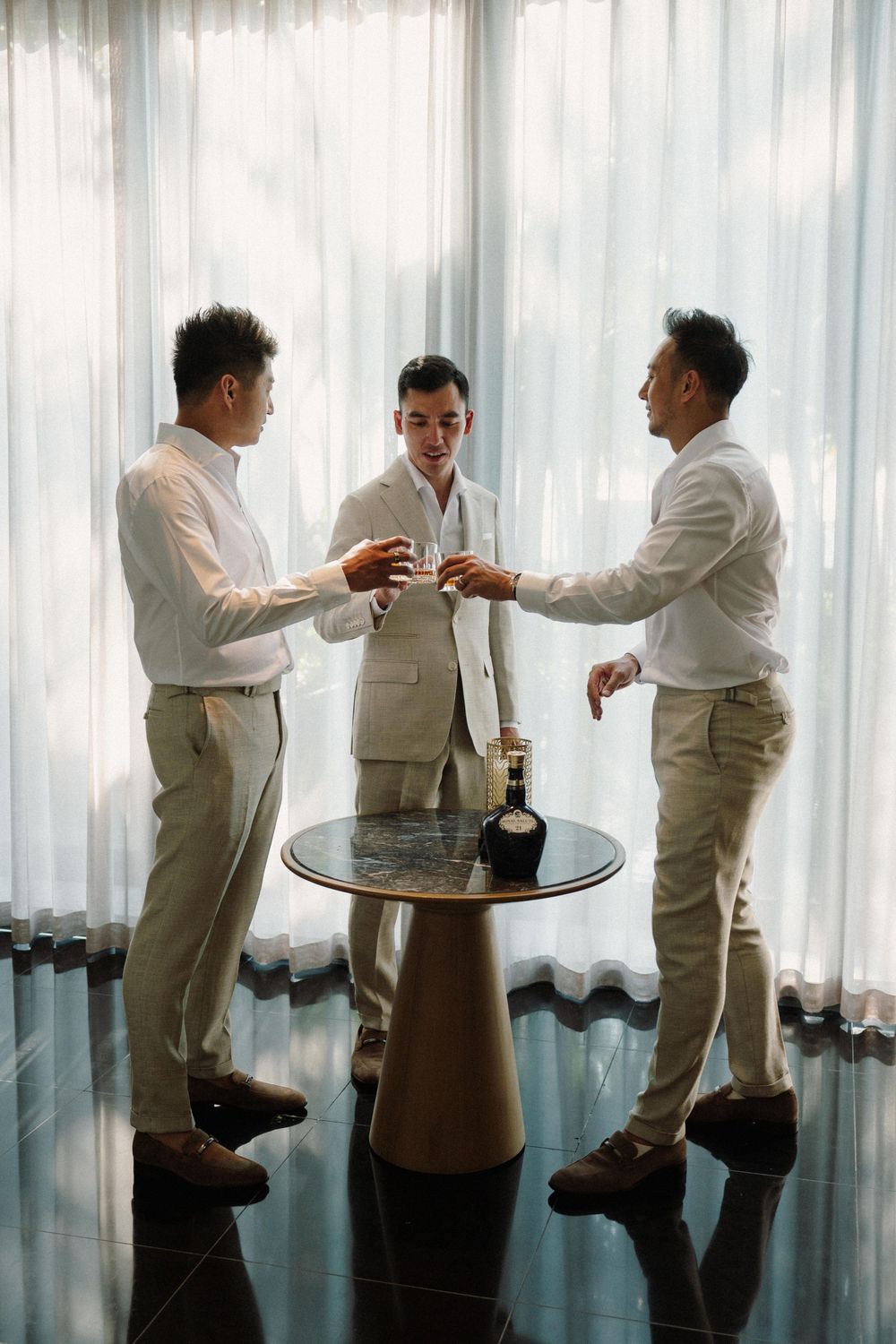 A sequence of men in white attire toasting and celebrating in front of sheer curtains.
