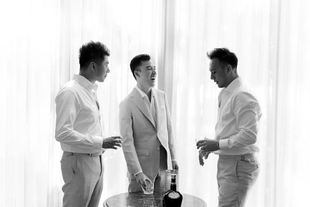 Groomsmen in formal attire preparing for a wedding in front of white curtains.