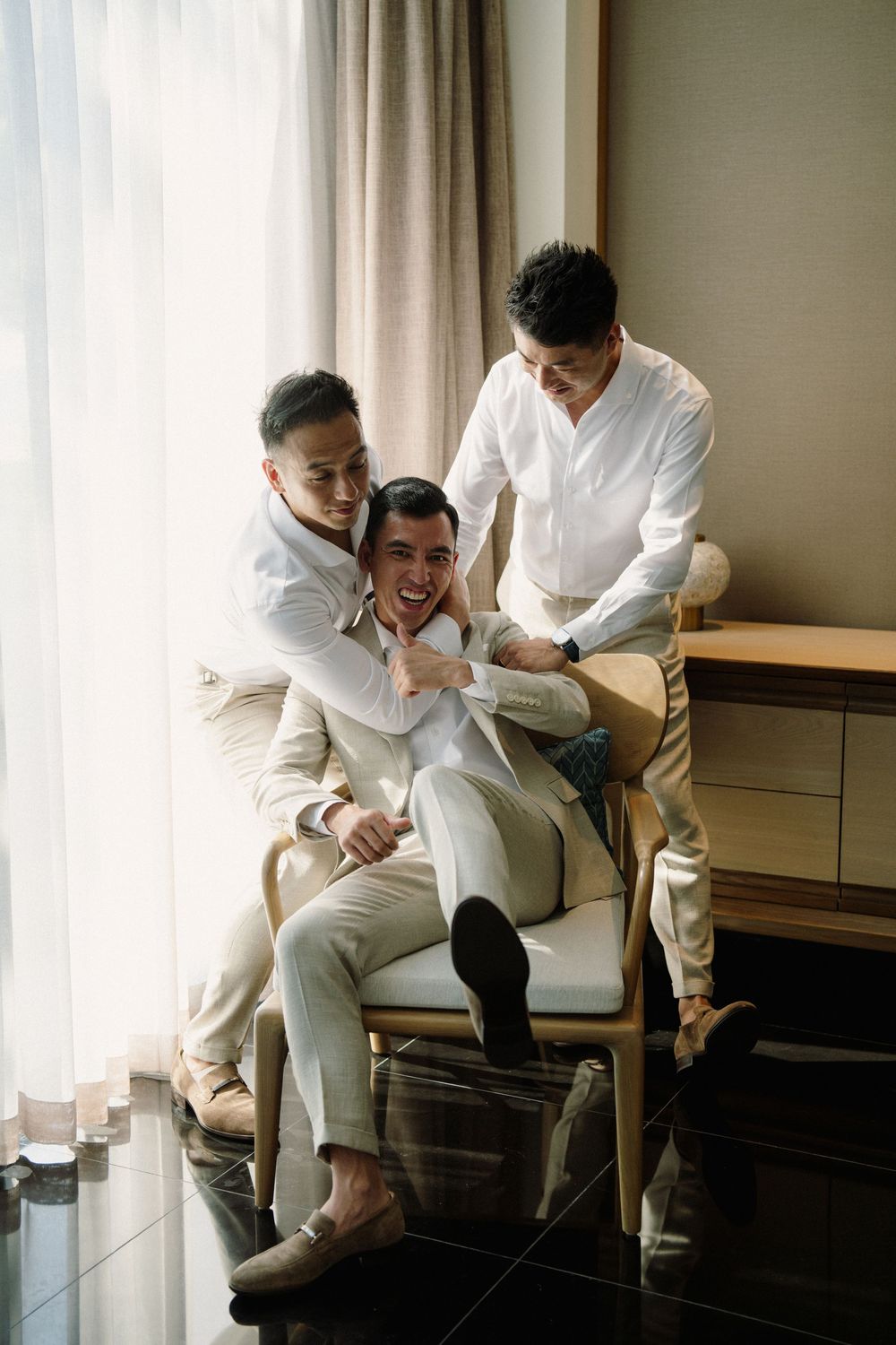 Four sequential photos show two people in white outfits sharing playful moments while sitting on furniture indoors.