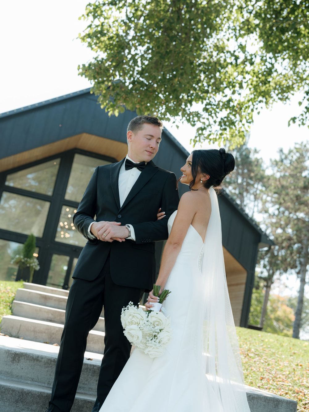 A romantic wedding couple shares an intimate moment on outdoor steps surrounded by greenery.