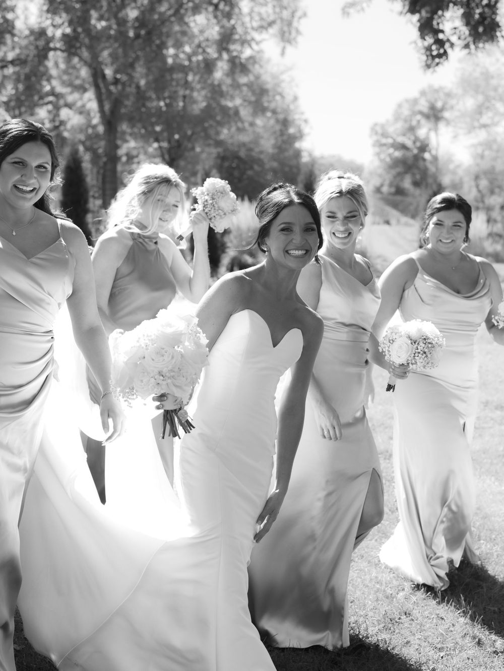 Black and white photo showing bridesmaids in white dresses laughing and posing playfully outdoors.