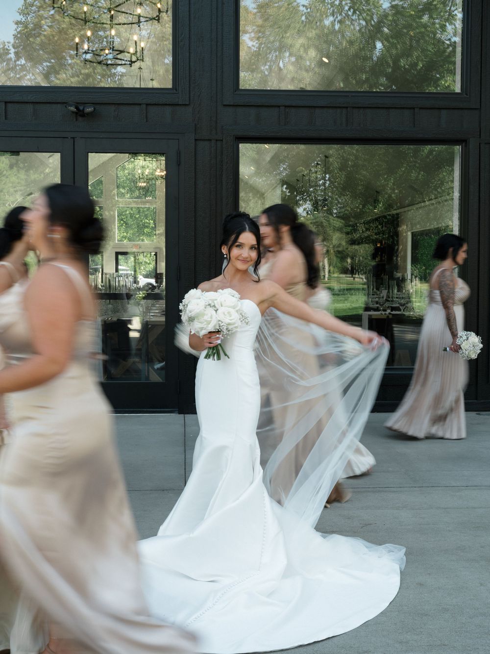 Bride and bridesmaids twirling and dancing in flowing dresses at an indoor venue.