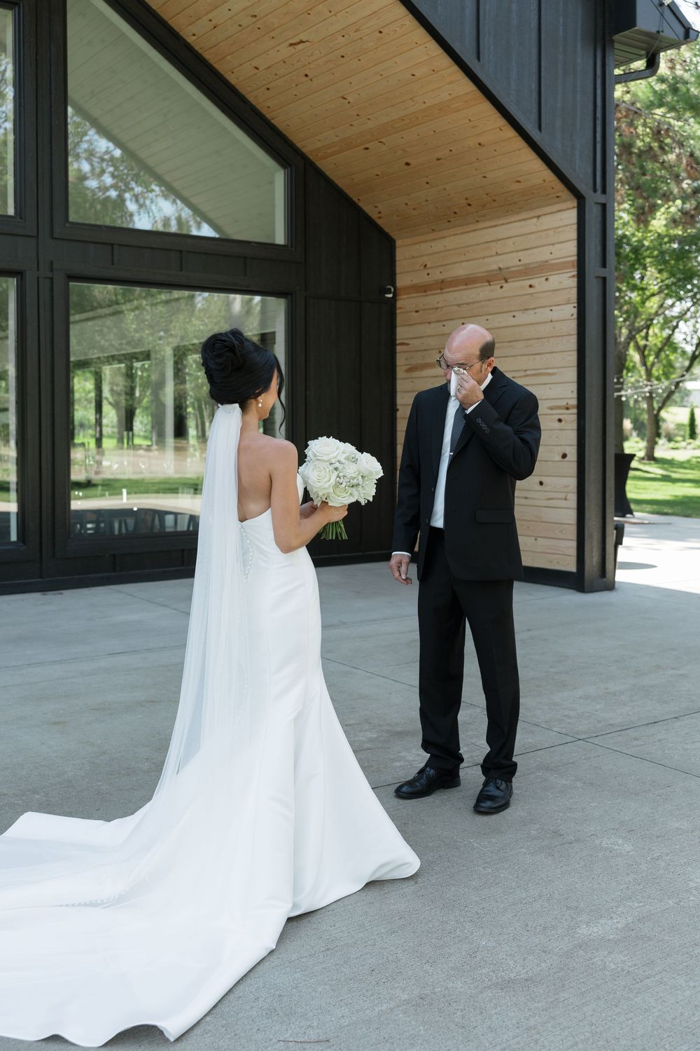 First look wedding moment captured at a modern wooden and glass venue with dramatic lighting.