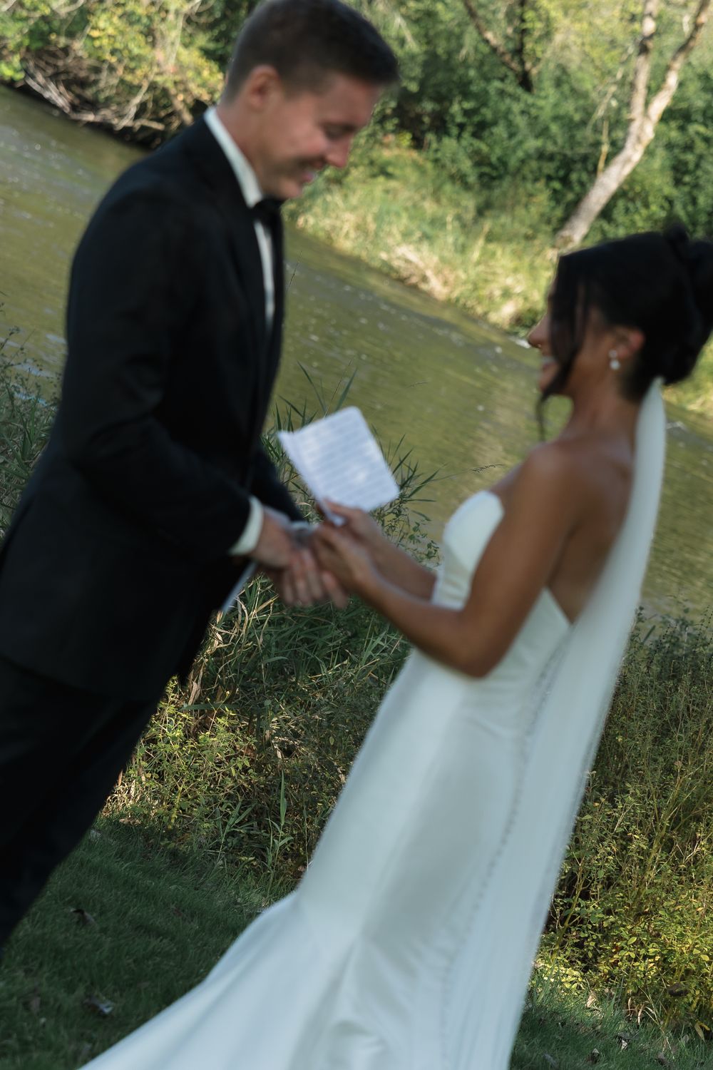 Wedding couple poses together in a natural outdoor setting near a river.