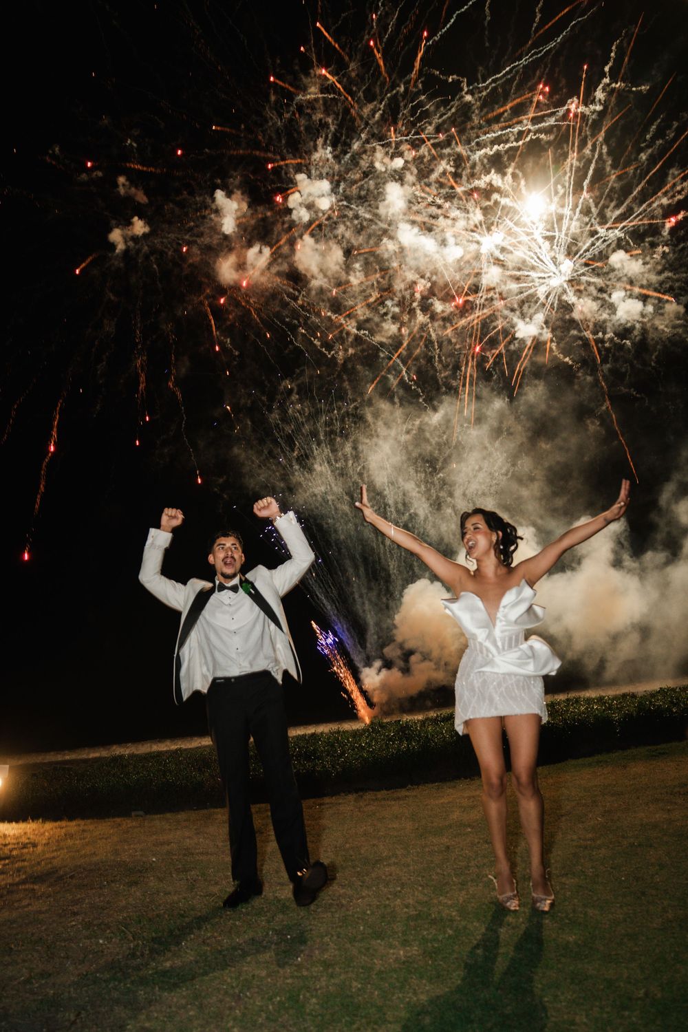 A couple dances joyfully under sparklers at night during an outdoor celebration.