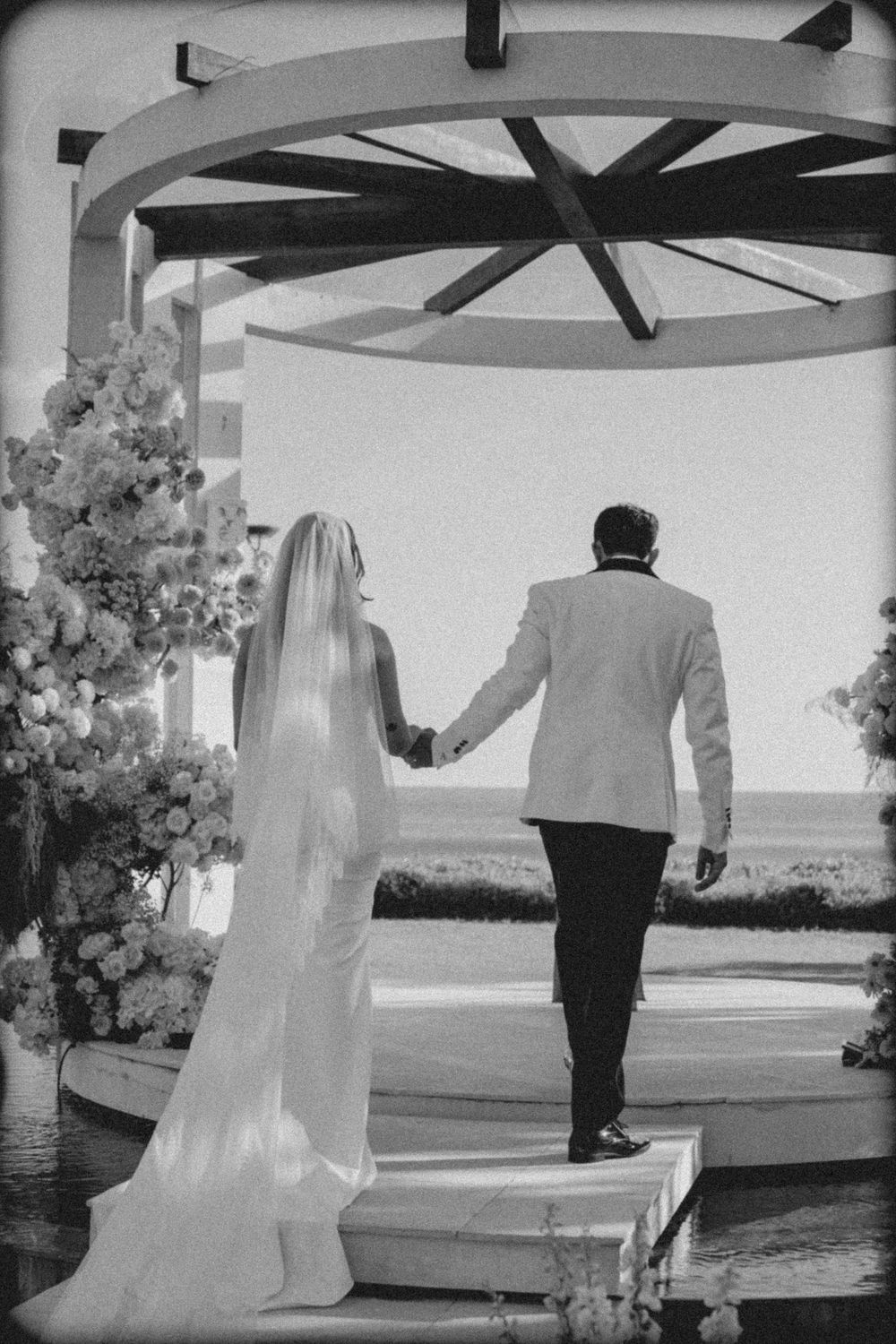 Black and white wedding photo series showing couple walking together under outdoor pergola with scenic view.