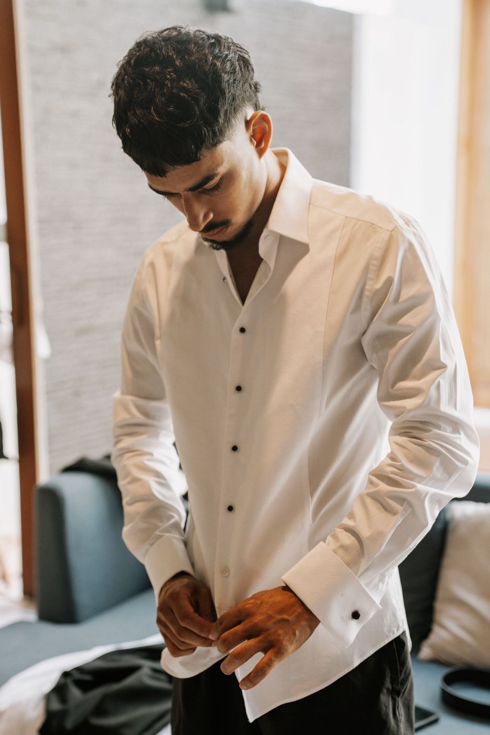 A person wearing a crisp white dress shirt adjusts their cufflinks while getting dressed.