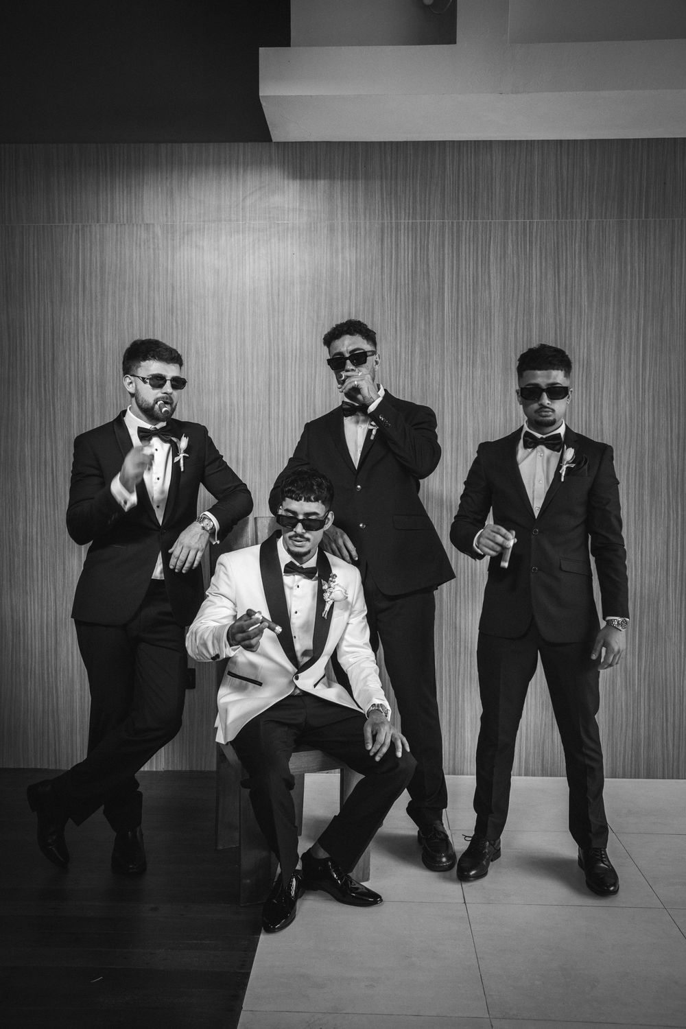 A black and white photo series showing a group in suits and sunglasses posing dramatically against a wall.