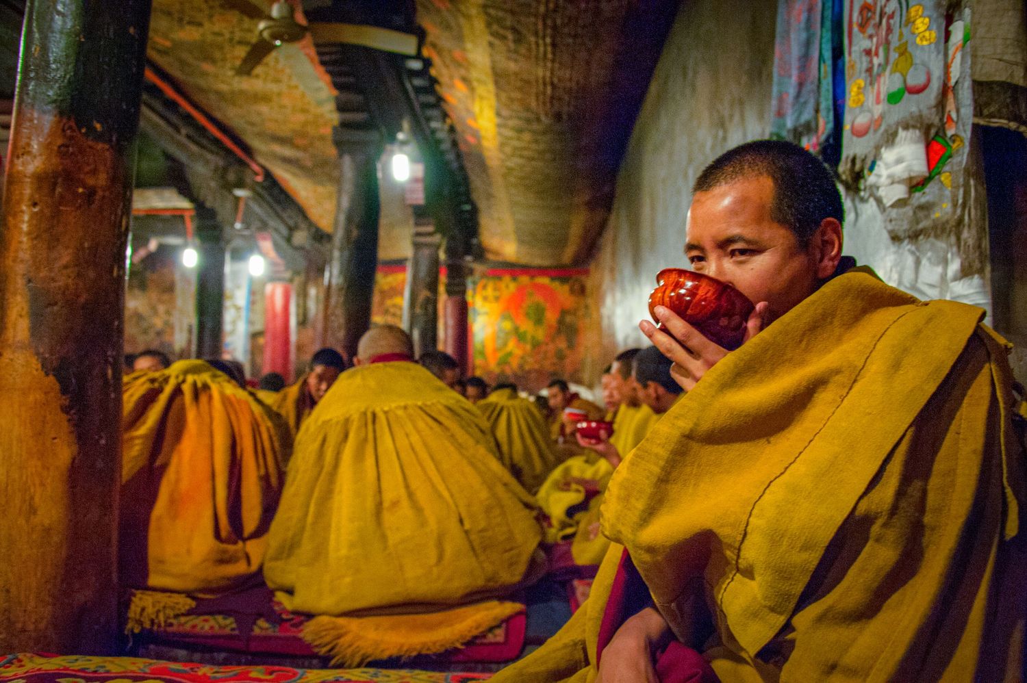 Buddhist monks in saffron robes gather at a dimly lit temple for a traditional ceremony.