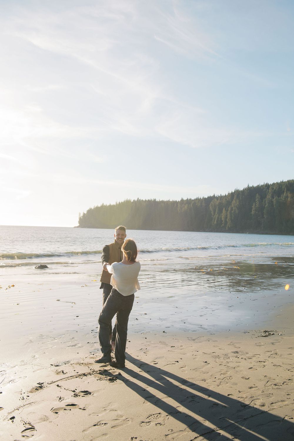 A couple casts dramatic shadows while enjoying a playful moment on a peaceful beach.