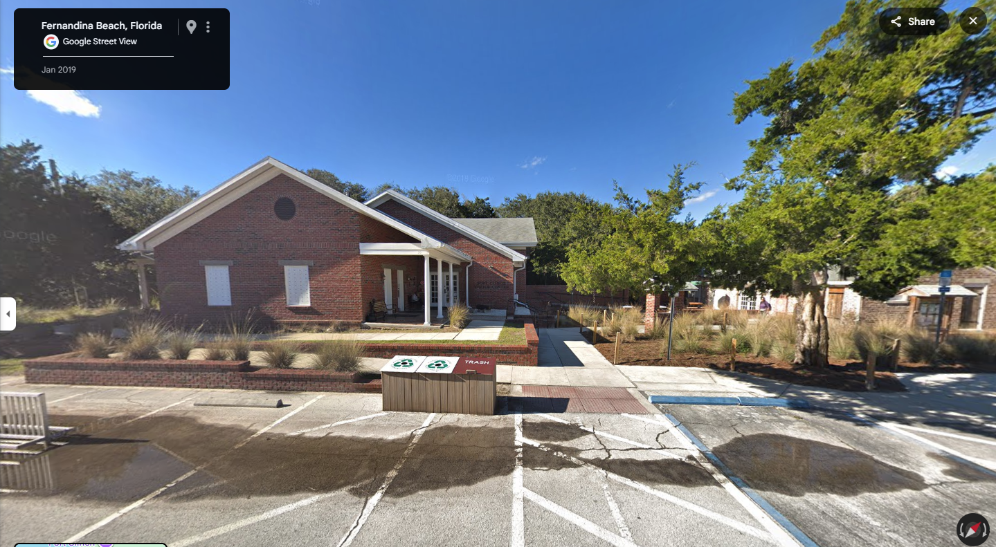 A brick building with a flat roof and landscaped entrance sits in a sunny Fernandina Beach parking lot.