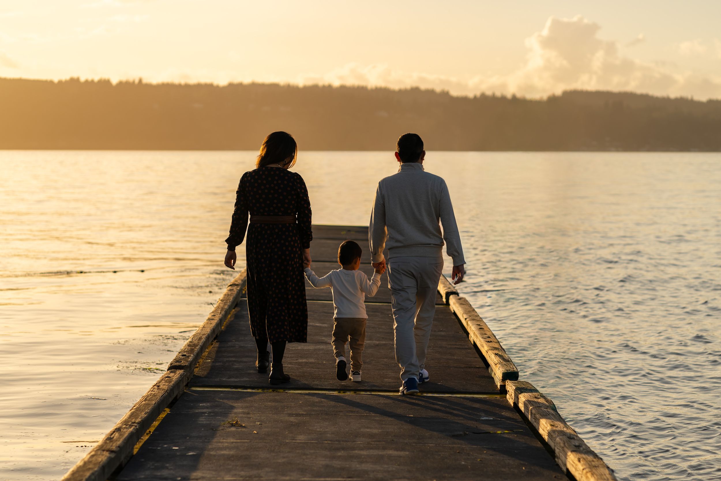 Family holding hands and walking on pier by the water in Mukilteo.