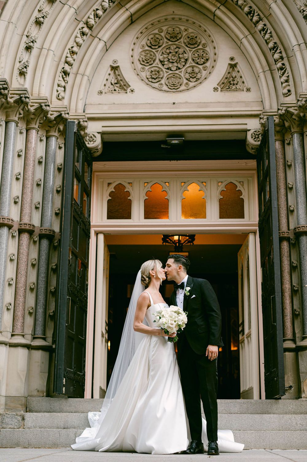 Elegant couple shares romantic moment in front of ornate Gothic stone St. Patrick Catholic church entrance.