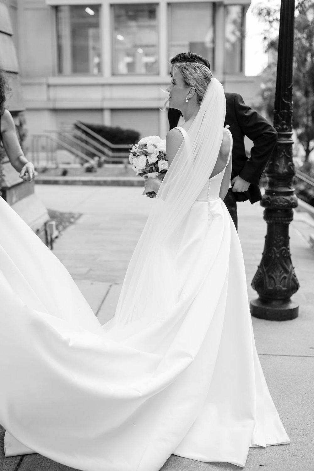 A bride in a flowing white wedding dress twirls gracefully on a city street, creating elegant movement with her gown.