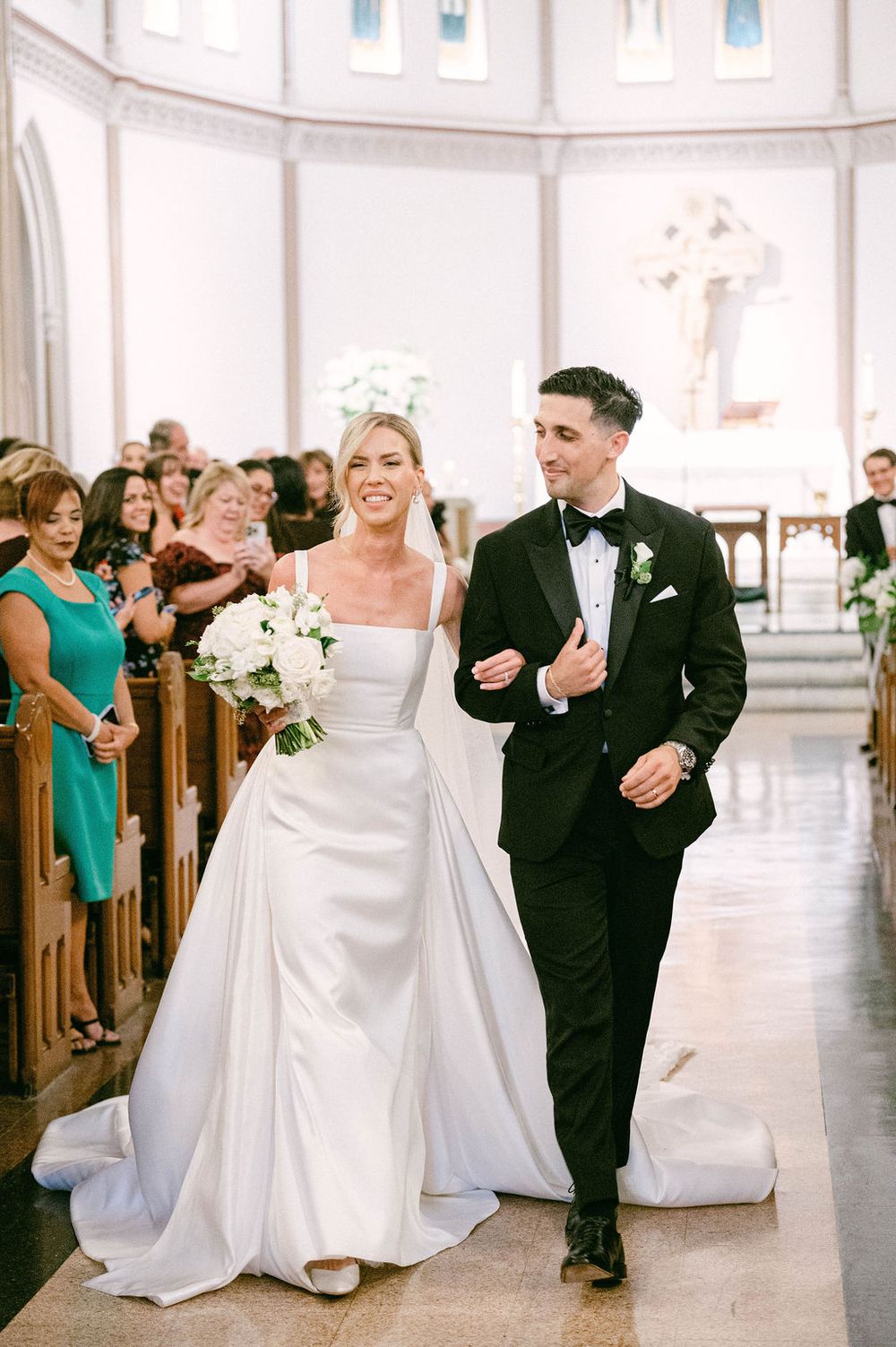 A bride and groom walk down the main St. Patrick Catholic church aisle with white columns and wooden pews.