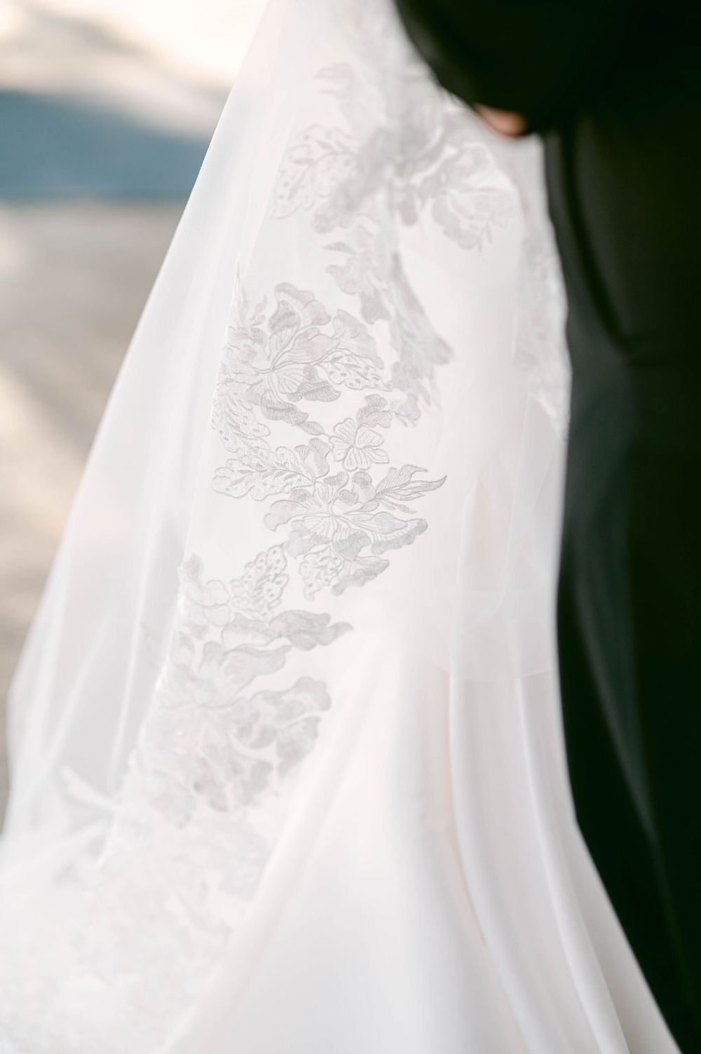 Close-up detail of delicate white lace embroidery on flowing wedding dress fabric.