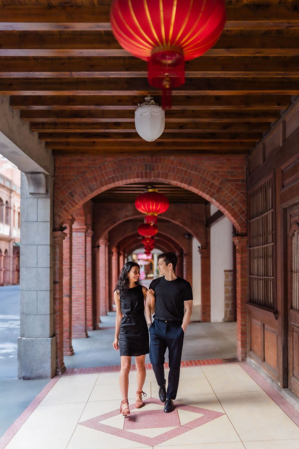 A couple strolls through a traditional Chinese archway corridor decorated with red lanterns at Taipei City's famous Dihua Street.
