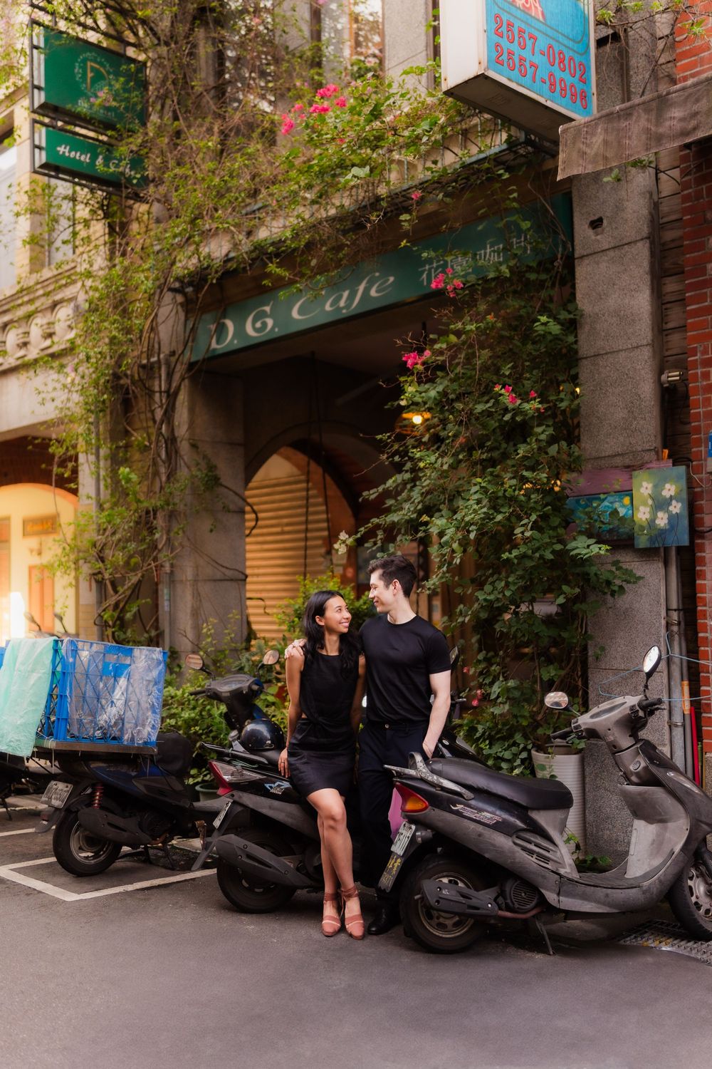 People gathered near parked scooters outside a cafe entrance with climbing vines and greenery on historic Dihua Street in Taipei, Taiwan.