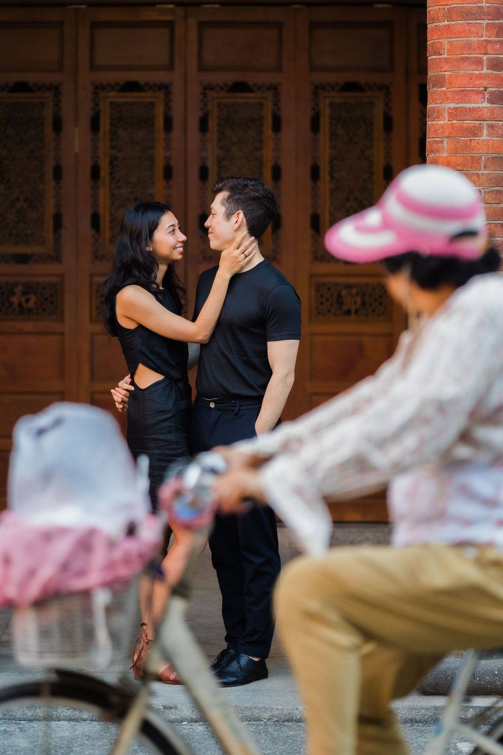 A tender moment shared by a couple on a street while a Taiwanese auntie cyclist passes by in the background.