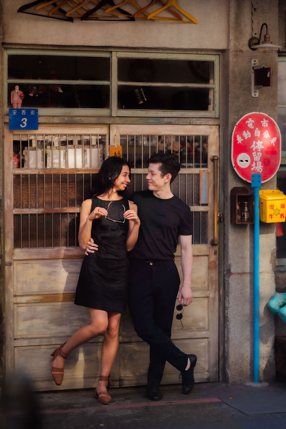 A couple poses playfully in front of industrial doorways and colorful signs on an historic Asian style urban street.