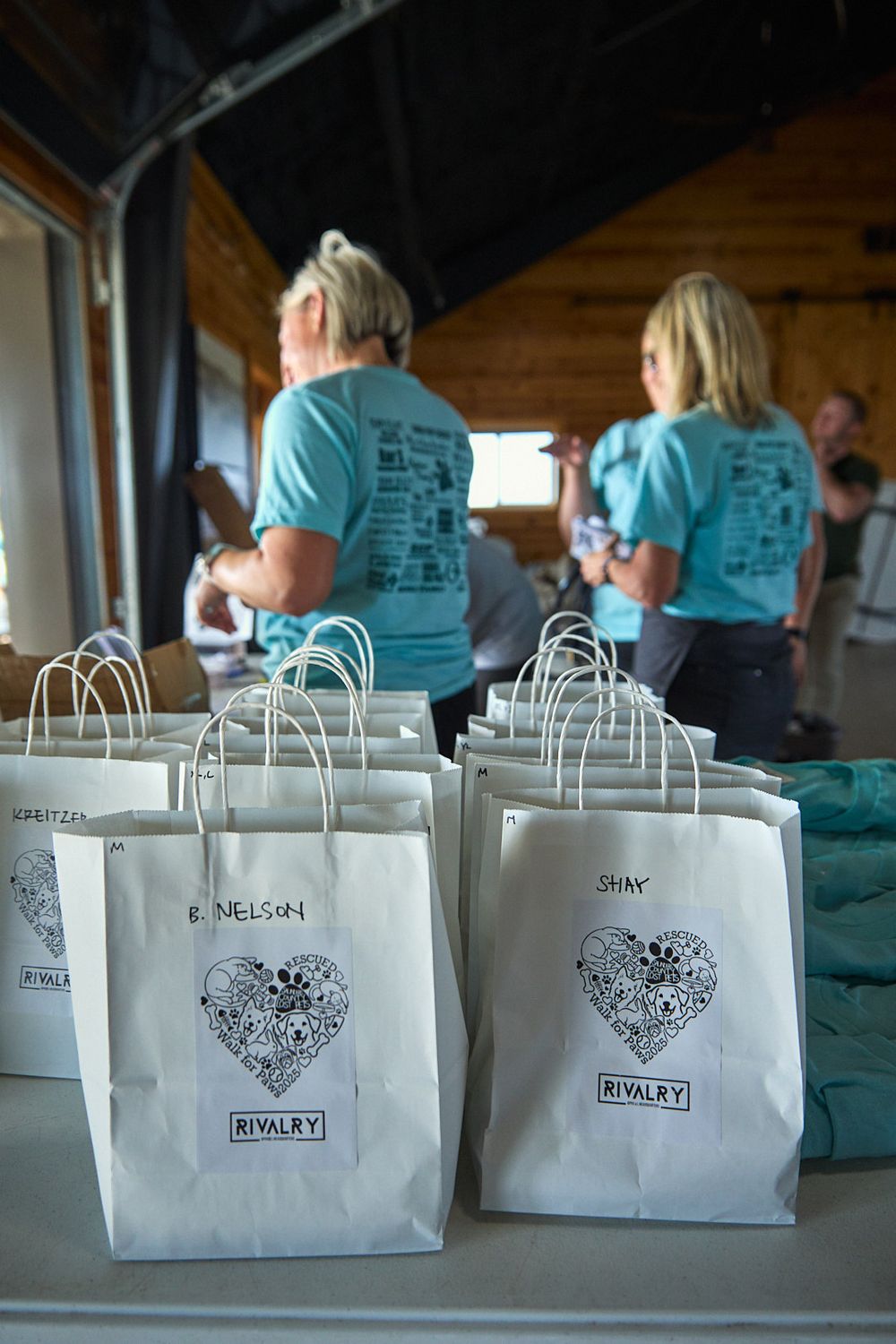 Row of white gift bags with heart designs lined up on a table at an event.