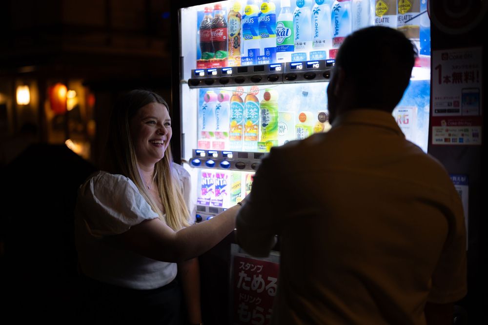 Woman smiling at her partner near a colorful Japanese vending machine glowing in the dark.