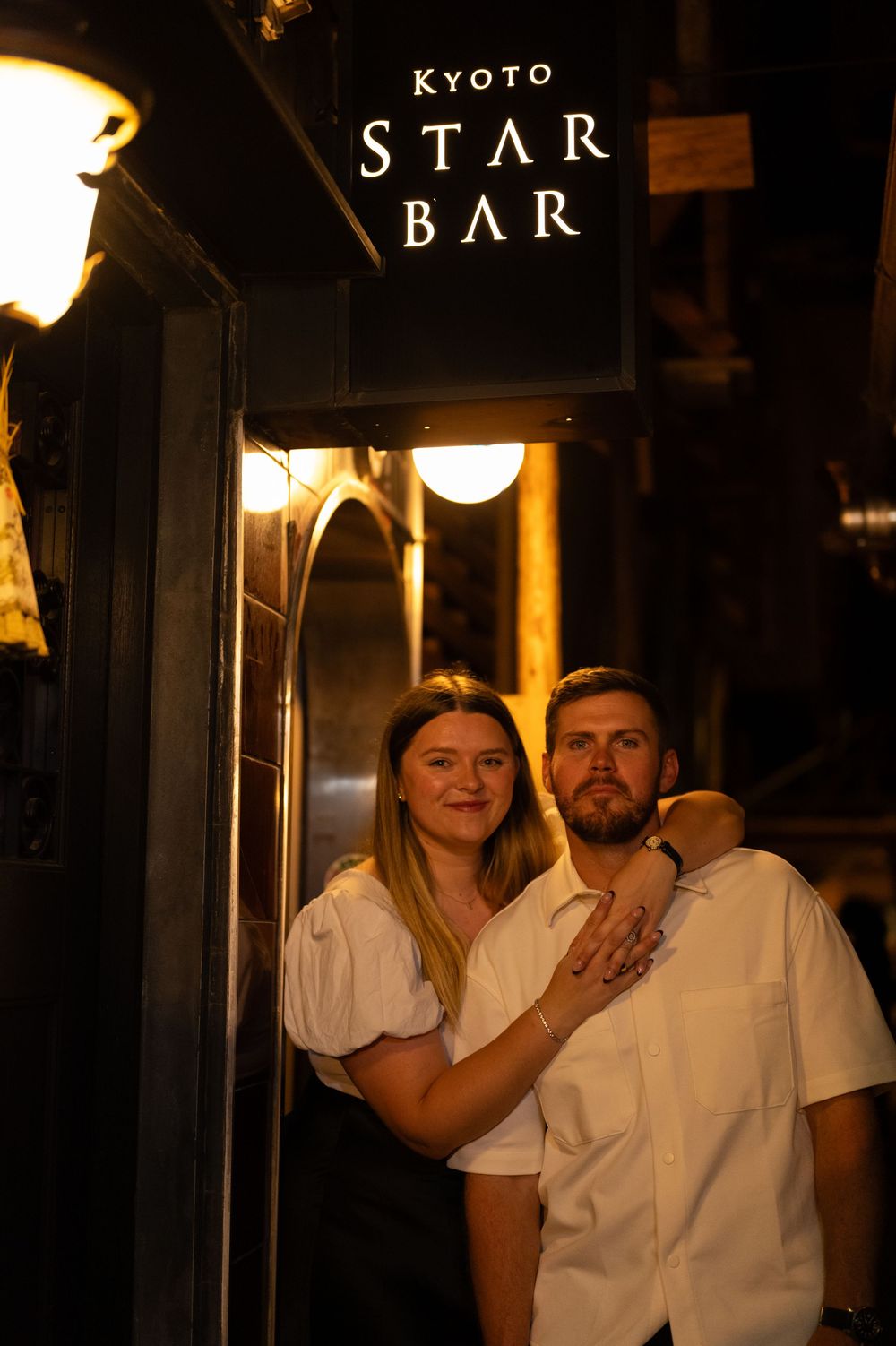Couple posing affectionately outside the Kyoto Star Bar beneath its elegant illuminated sign.