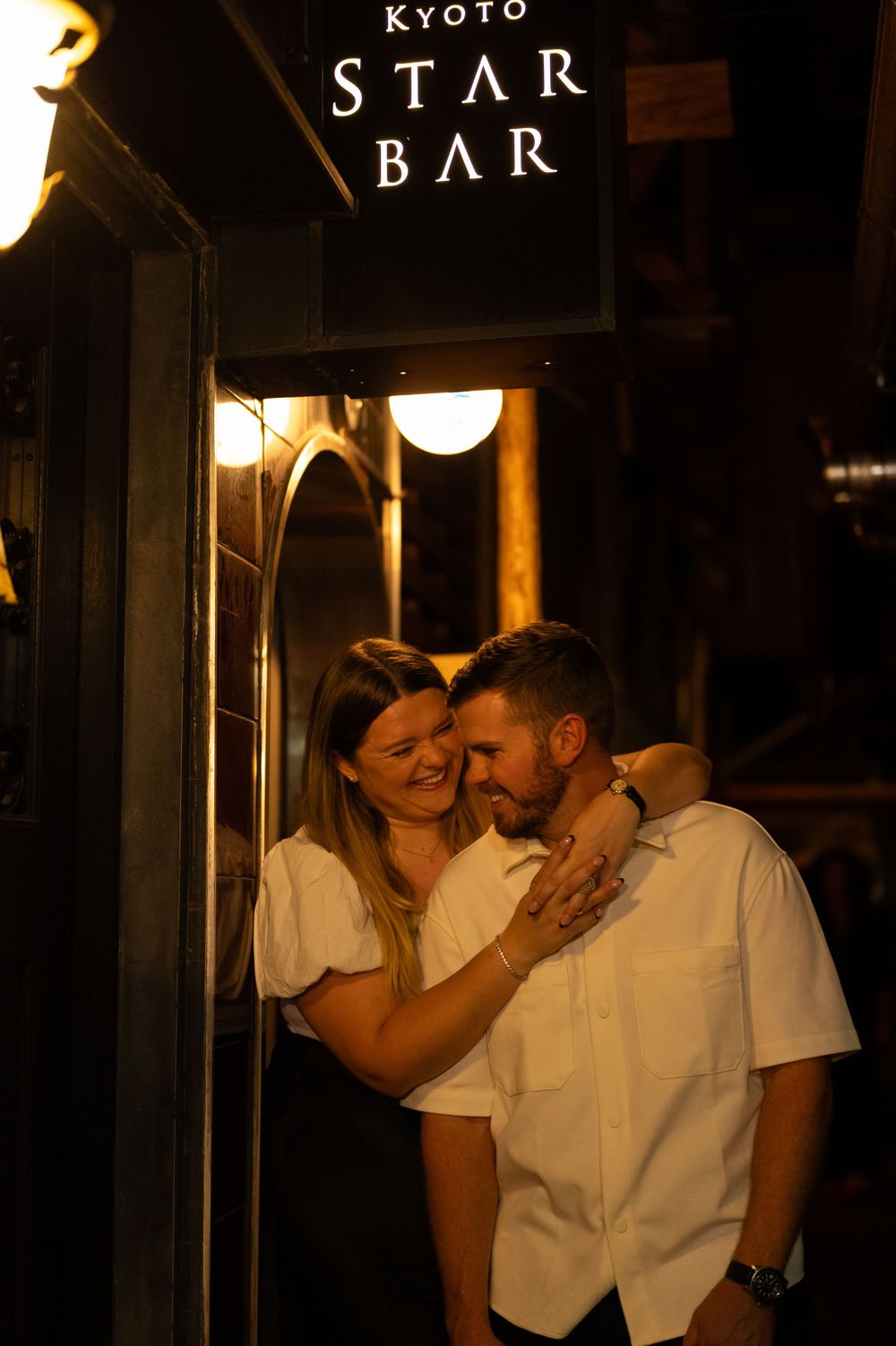 Couple laughing and embracing outside the Kyoto Star Bar under warm evening lighting.