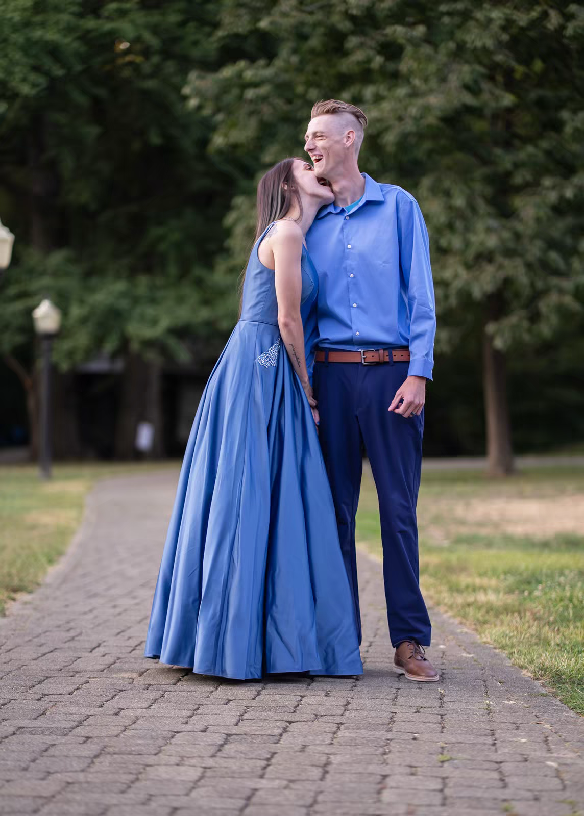 A couple in purple and blue attire pose dramatically on grass at dusk.