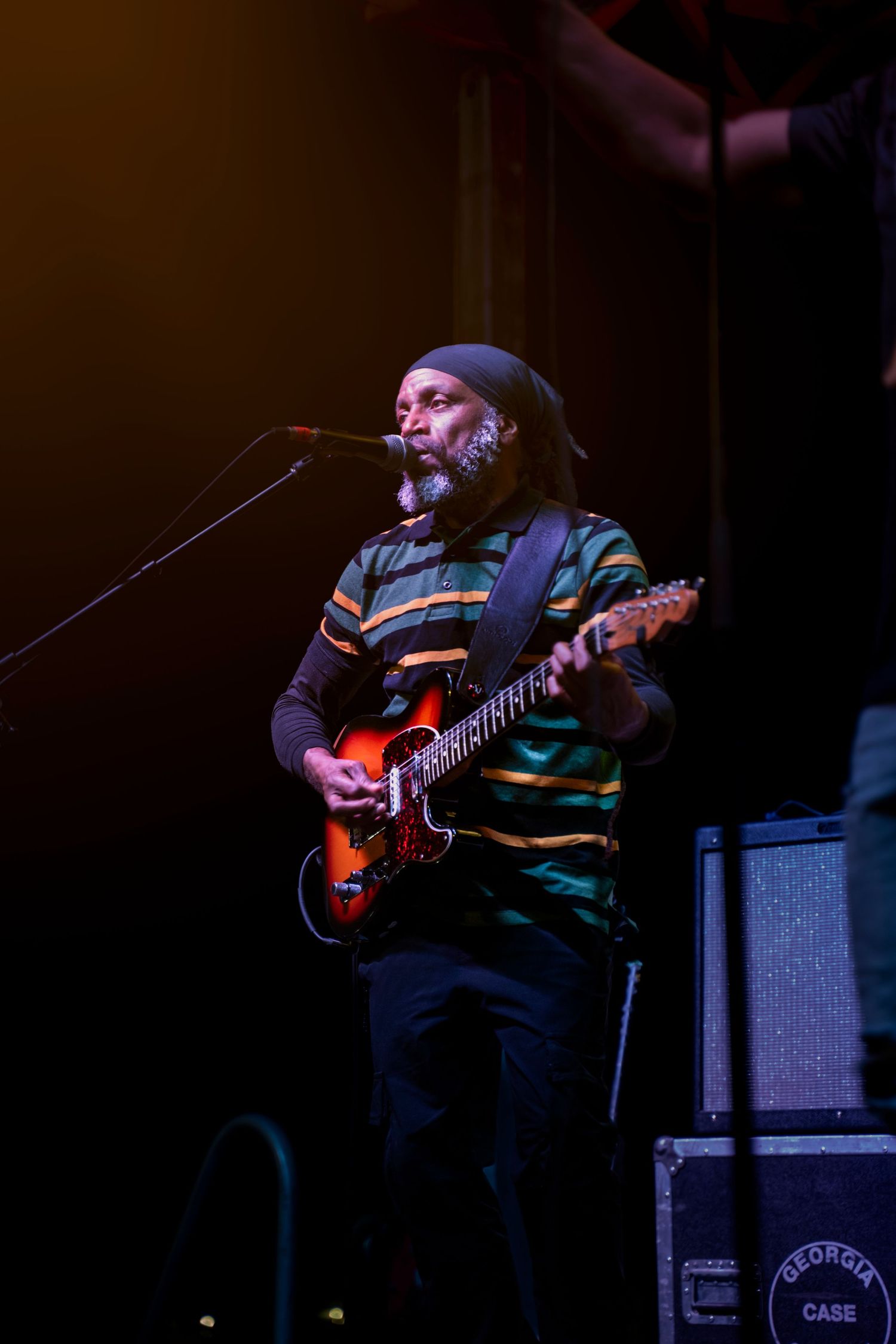 Blues guitarist performs on stage in dark lighting with an electric guitar and amplifier setup.