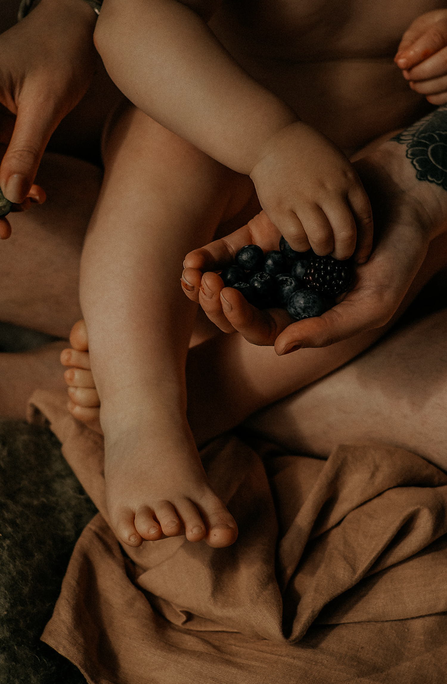 Close-up detail of a child’s legs and hands holding berries while sitting on soft fabric during a natural lifestyle family photography sessi