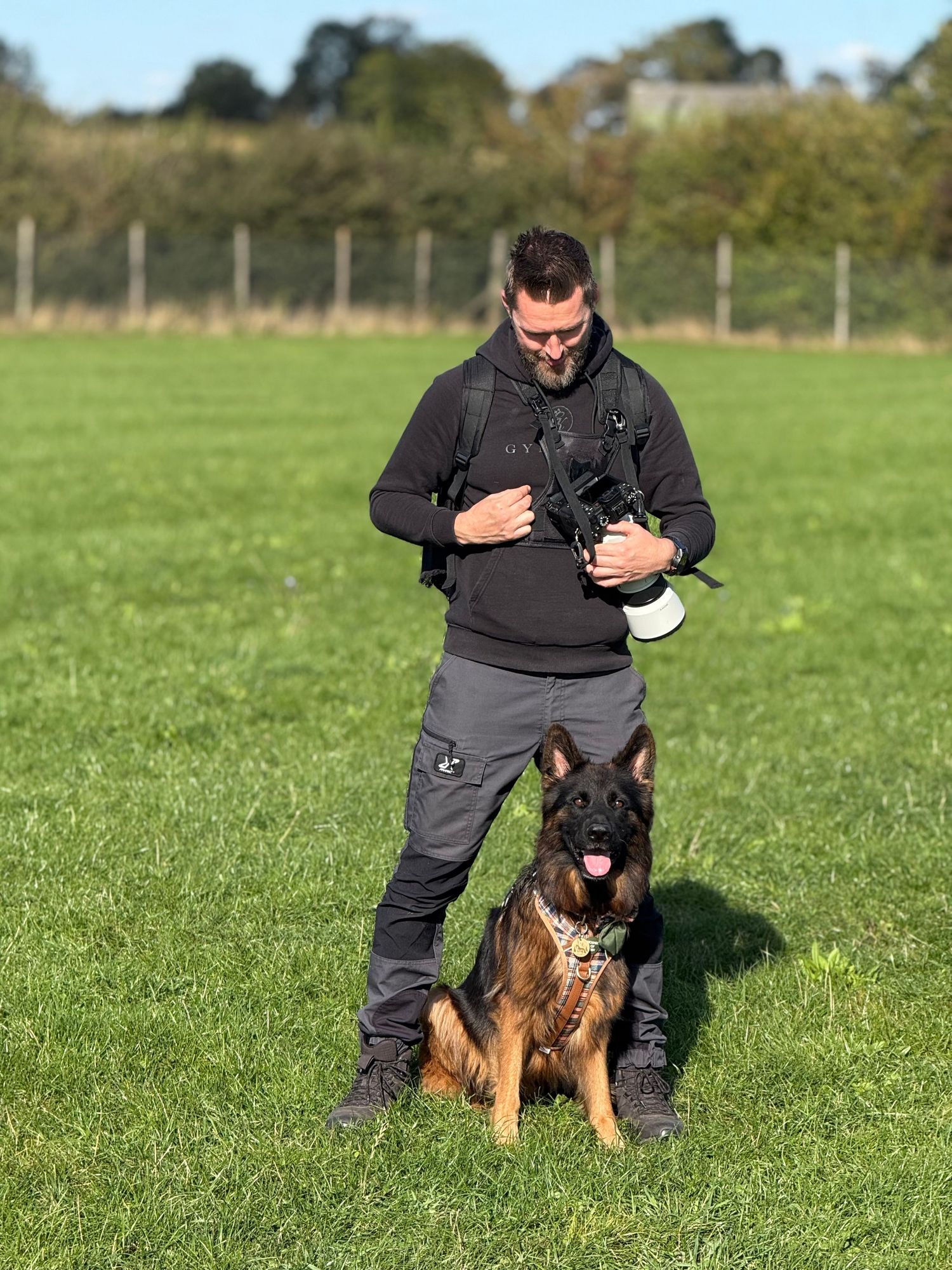A German Shepherd dog and companion pose together on a wooden platform in an outdoor training area.