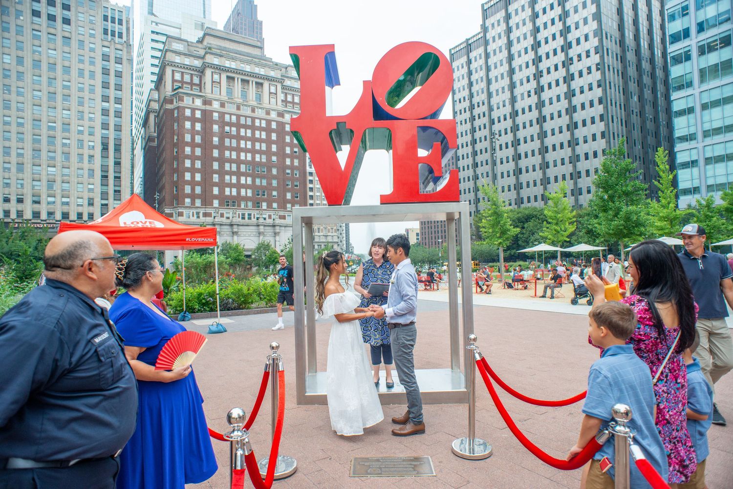 People interact with the iconic LOVE sculpture and red art installation in a city plaza surrounded by skyscrapers.