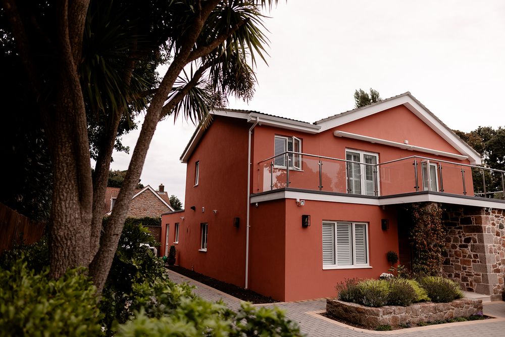 Exterior view of a coral-colored house with palm trees and lush landscaping.