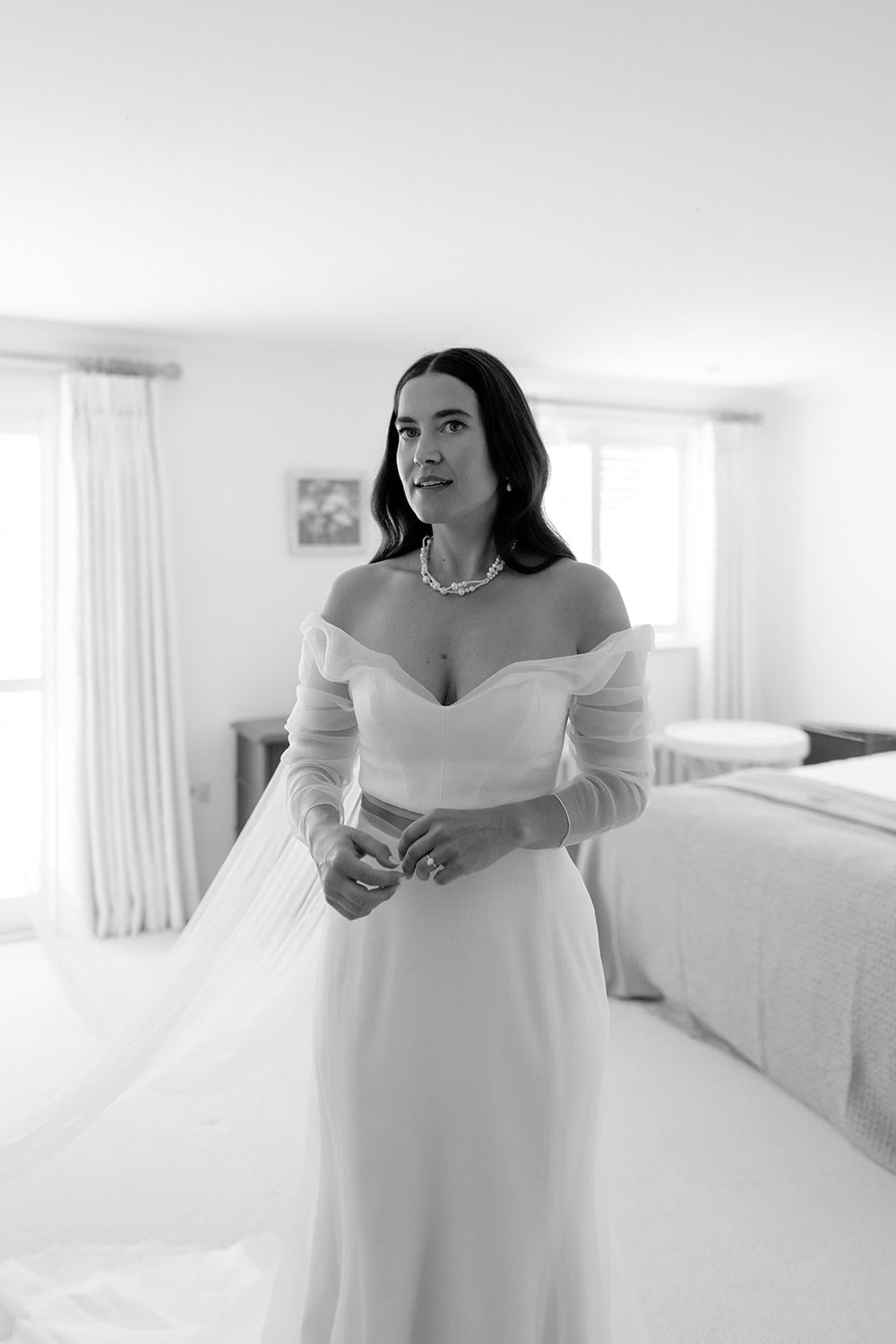 Person in an off-shoulder white wedding gown in a bright, minimalist room.