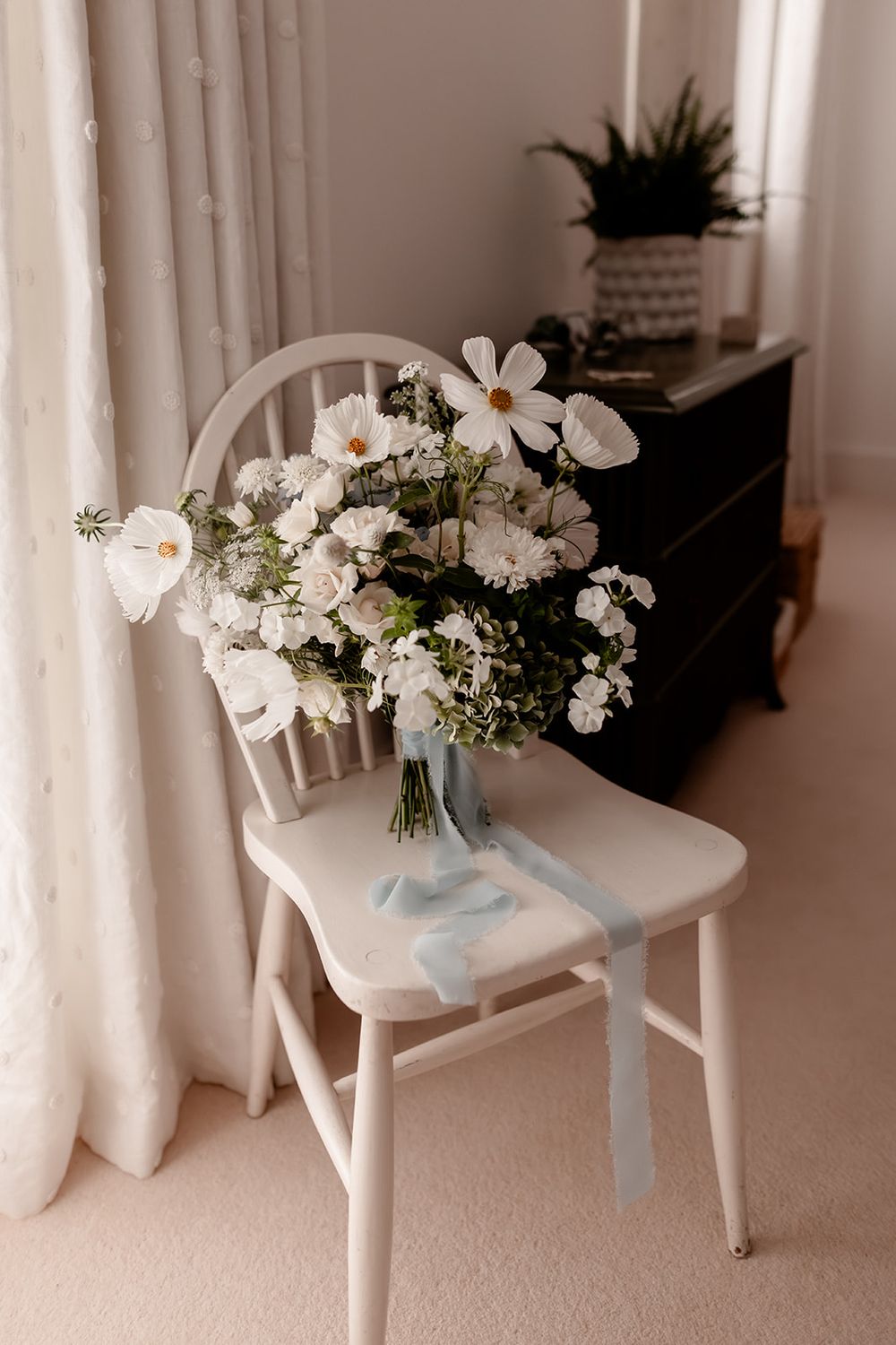 White floral bouquets with blue ribbons arranged on white wooden chairs.