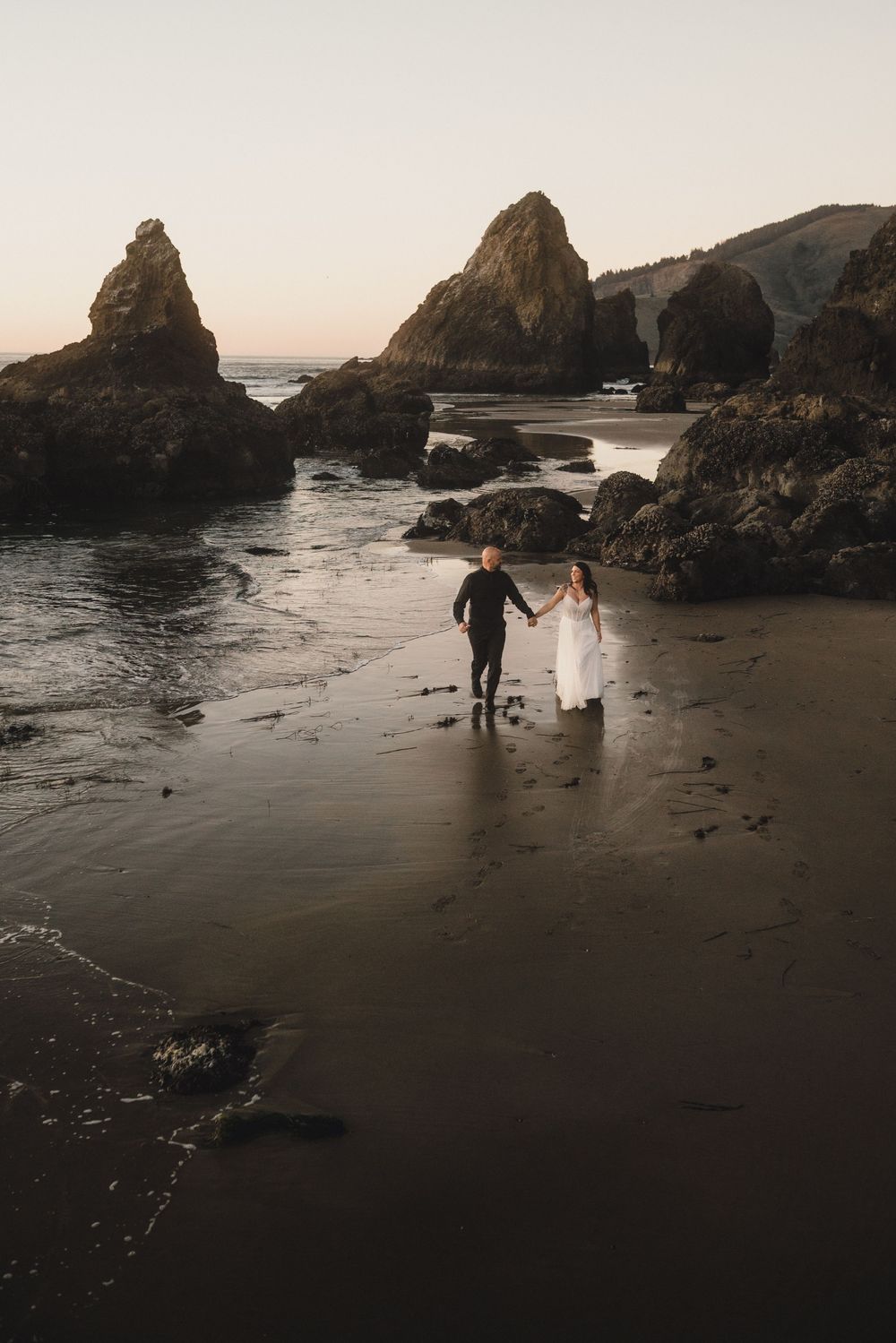 Silhouettes of people and a dog walking along a misty beach with dramatic rock formations at sunset.