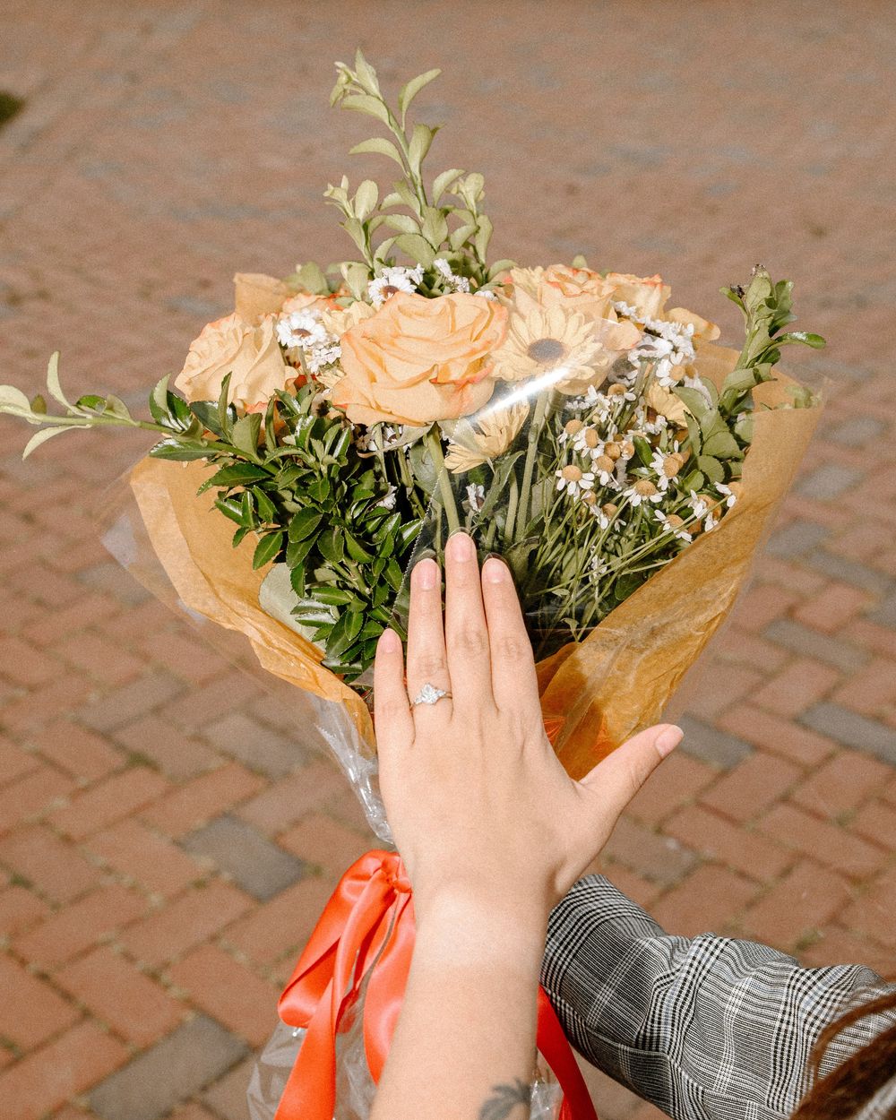 Close up of hands holding a bouquet of peach roses and white flowers wrapped in paper.