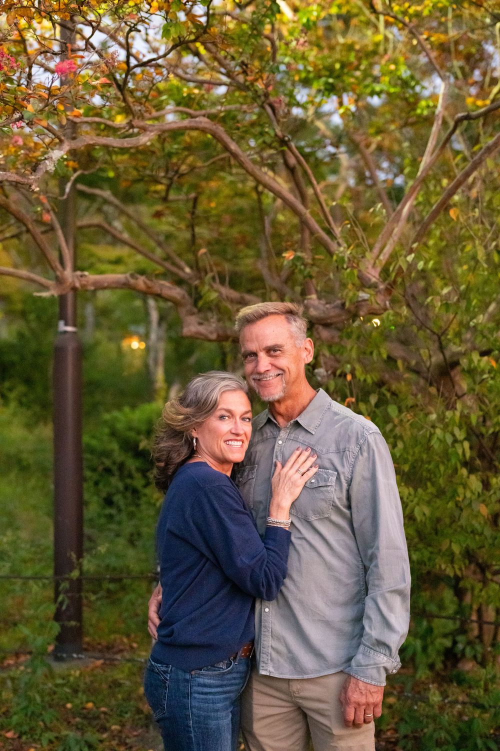 Mature couple smiling and embracing outdoors surrounded by lush autumn garden greenery.