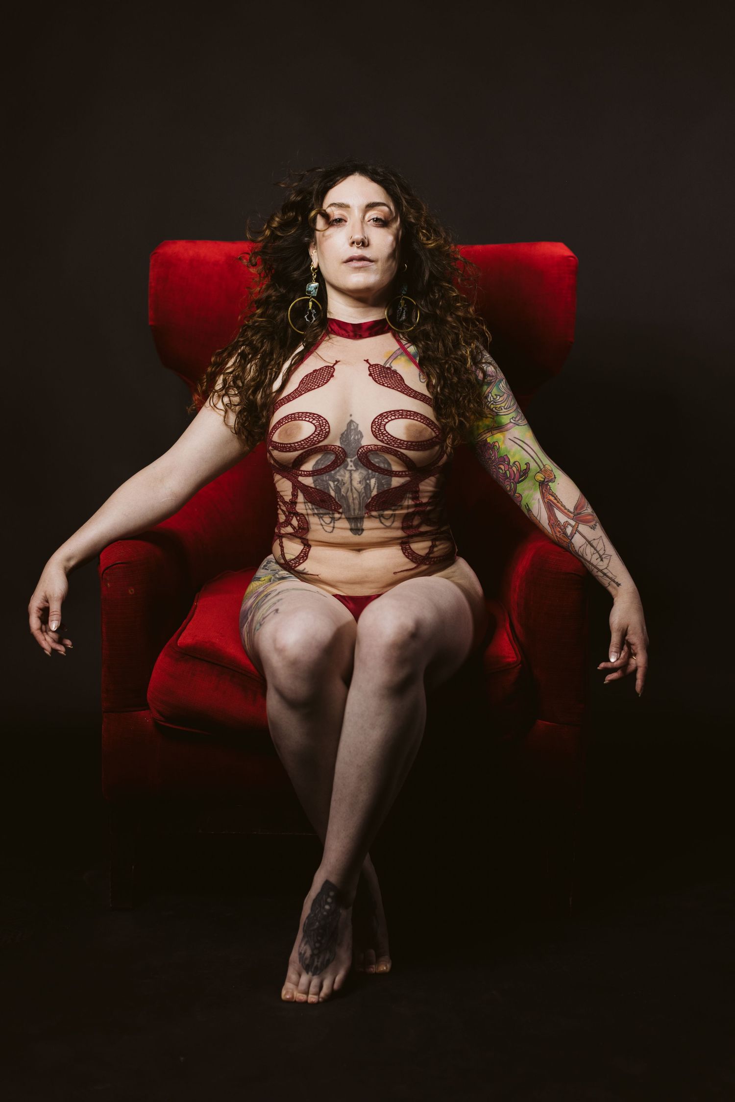 Dramatic boudoir photography series on red velvet couch with moody dark lighting.