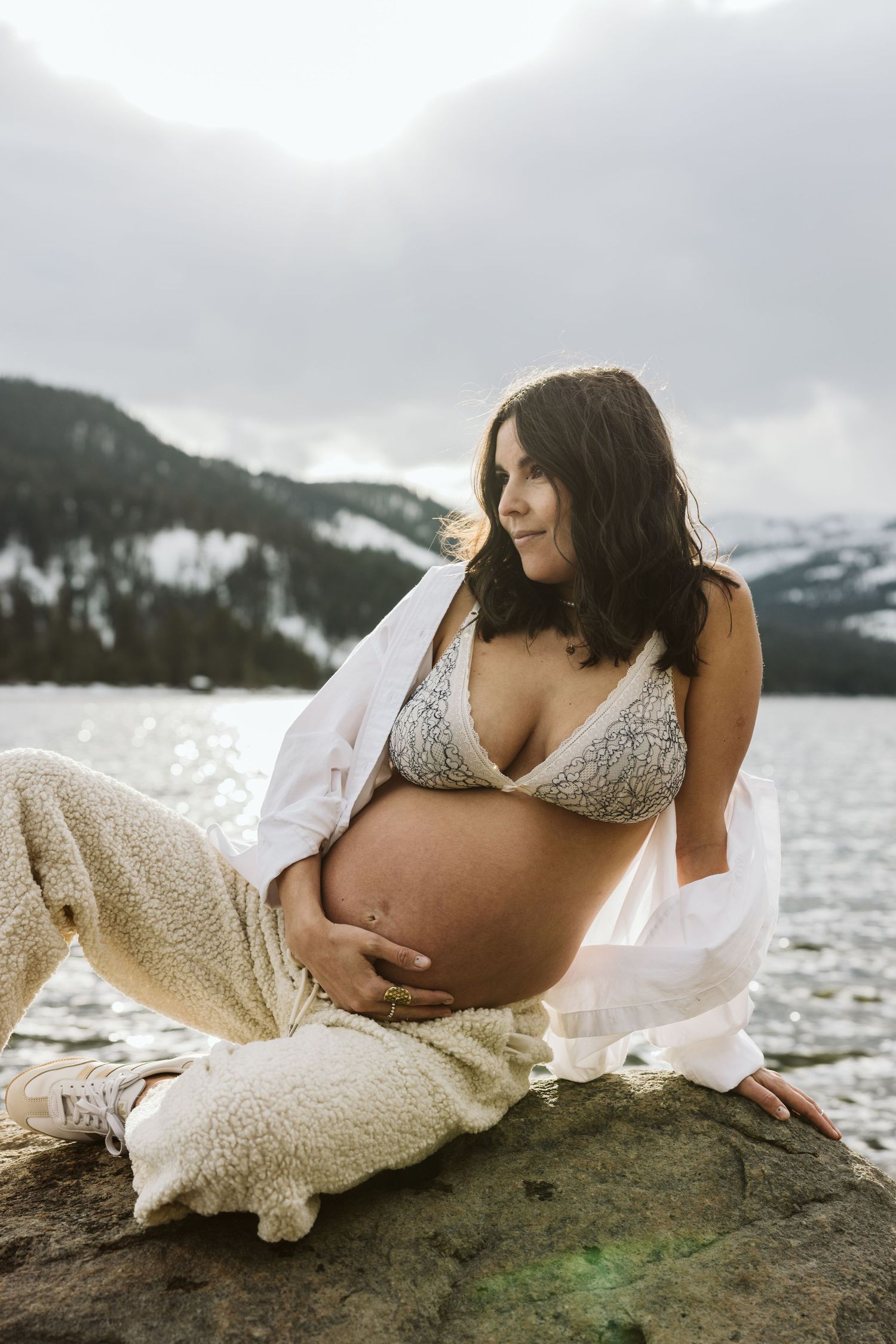 Maternity photo series showing intimate moments by a mountain lake with a person in white lace against mossy rocks.