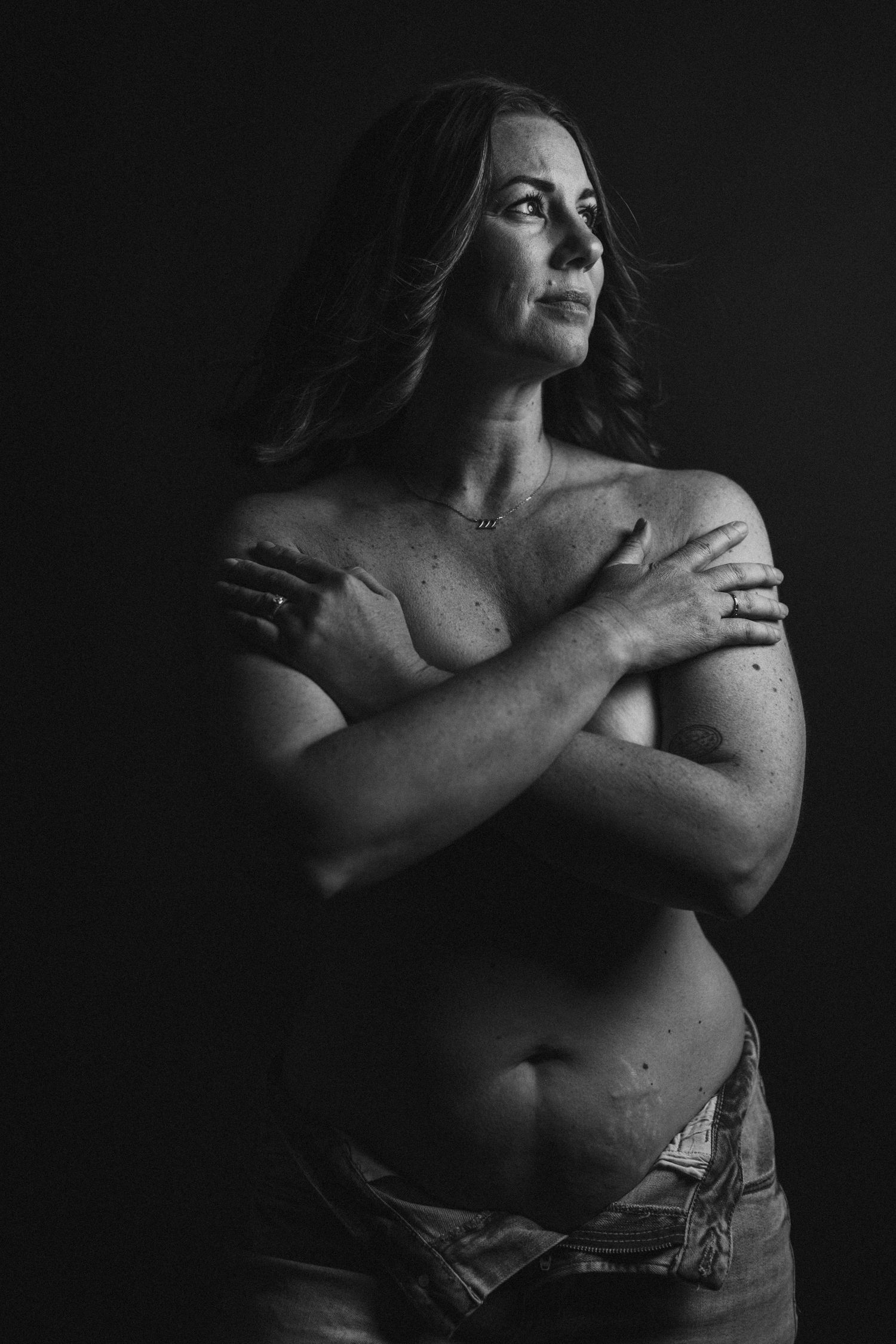 Dramatic low-key portraits showing intimate self-embrace poses in dark setting.