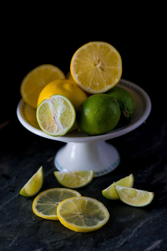 Fresh lemons and limes on a white cake stand with sliced citrus fruits.