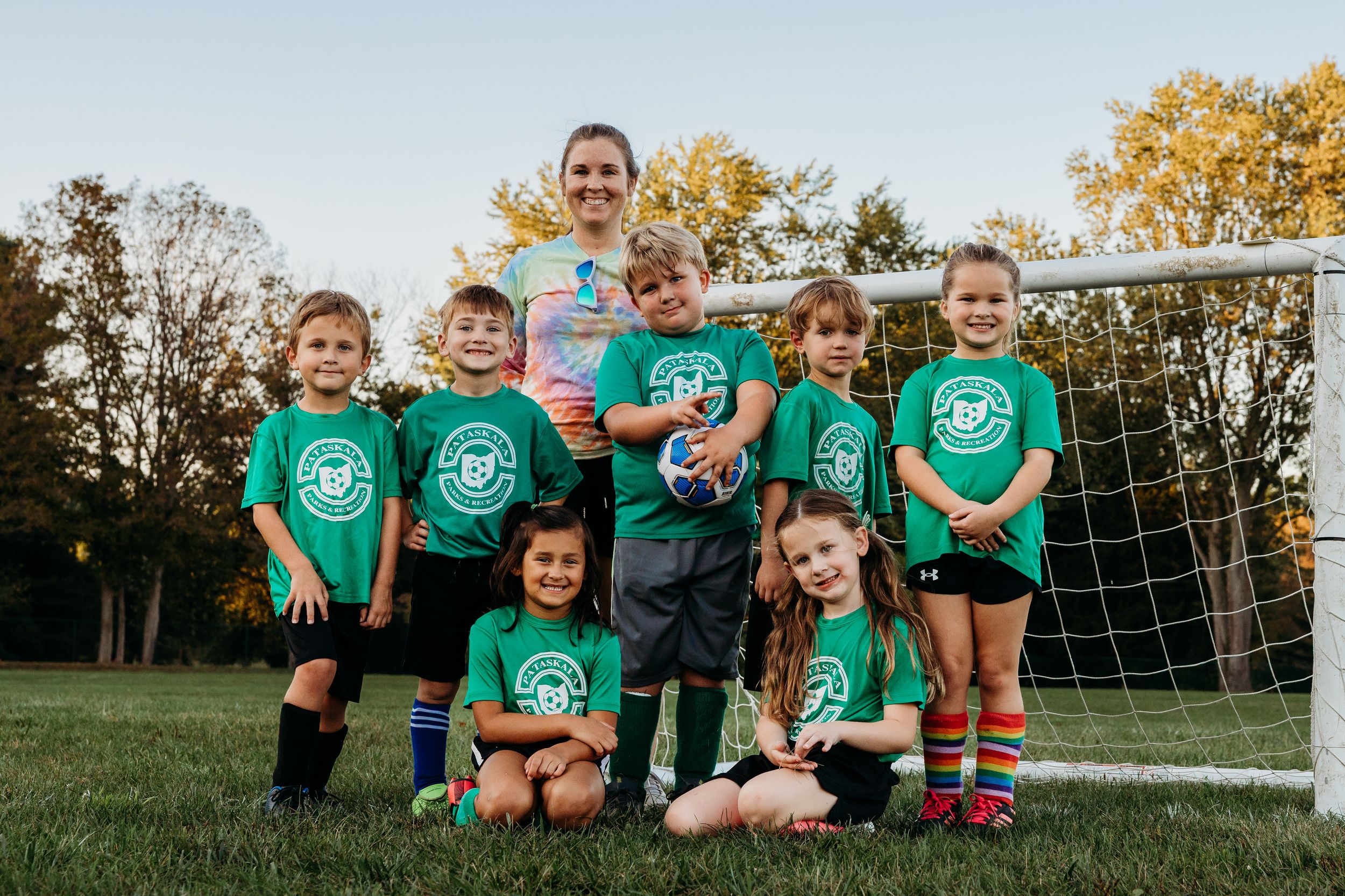 Youth soccer team in bright green jerseys poses together by goal posts during outdoor practice session.