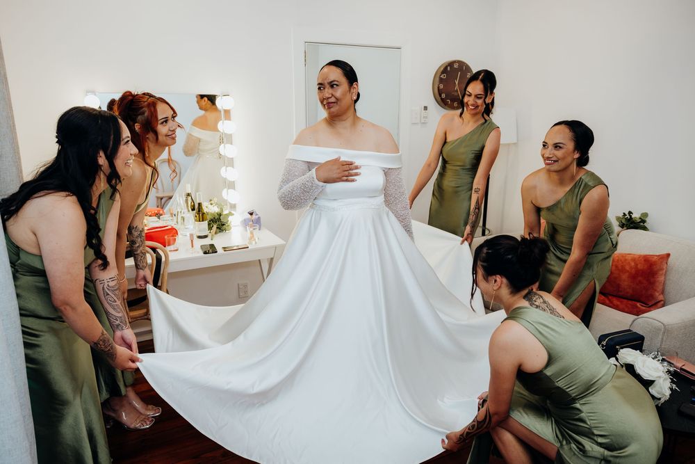 Bridesmaids in sage green dresses help adjust a wedding gown during pre-ceremony preparations.
