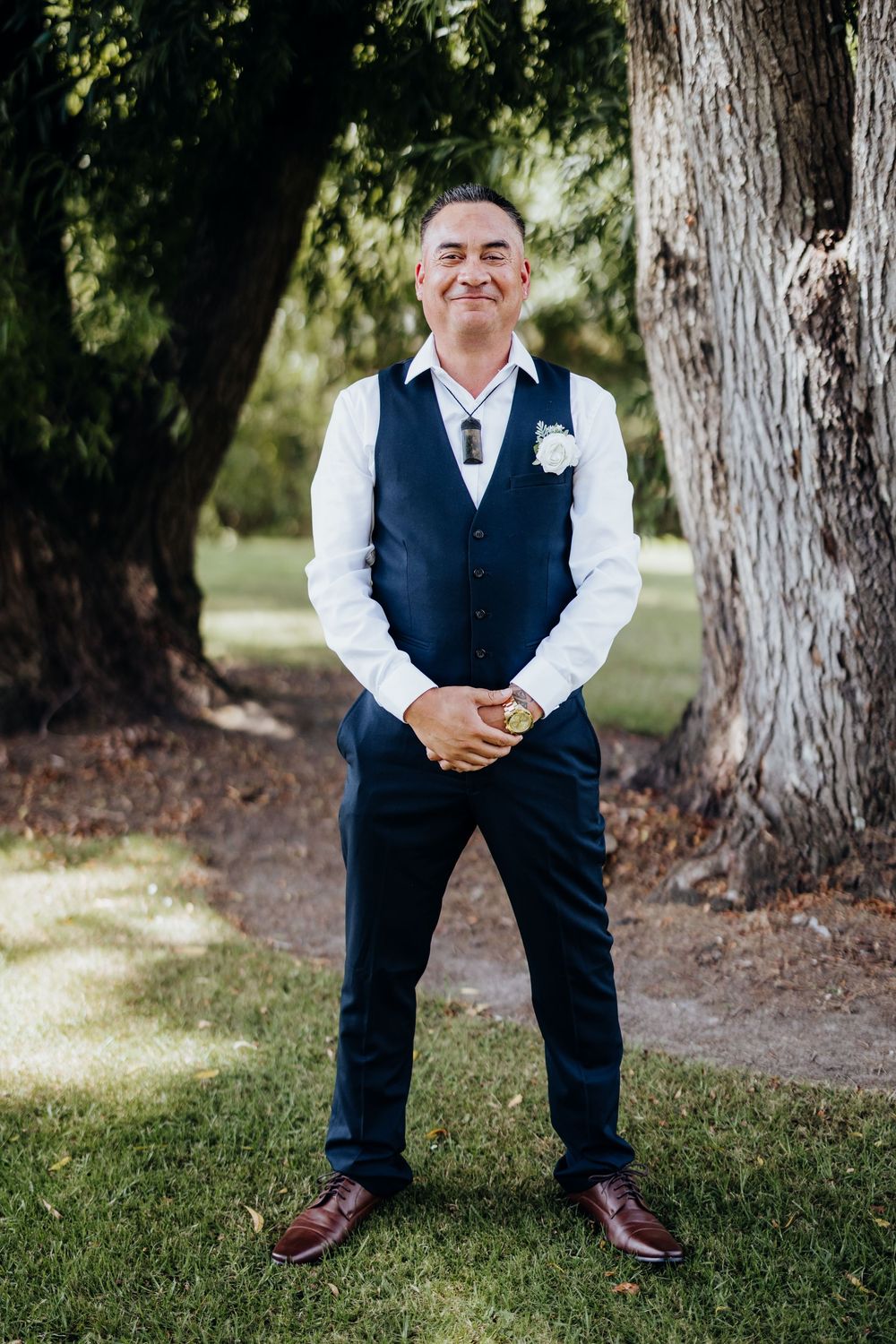 A person wearing a navy vest and white shirt poses playfully in a series of outdoor portraits near trees.