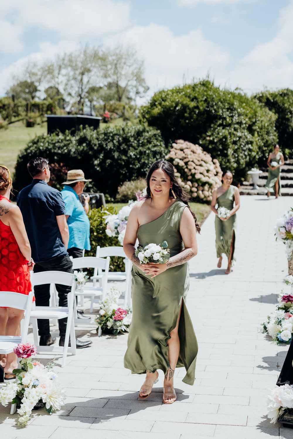 Wedding guests mingle on a white outdoor deck decorated with floral arrangements and white chairs.