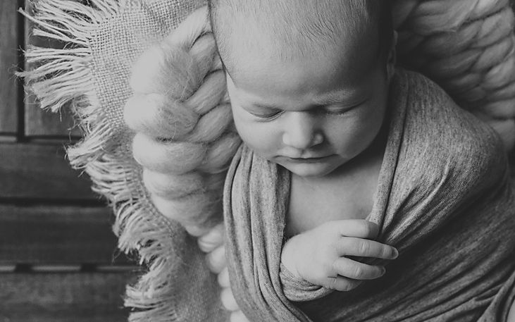 Monochrome portrait of sleeping newborn wrapped in soft fabric with textured background.