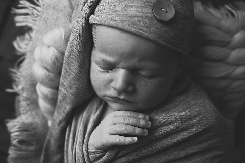 Black and white newborn portrait with textured wrapping and dramatic lighting.